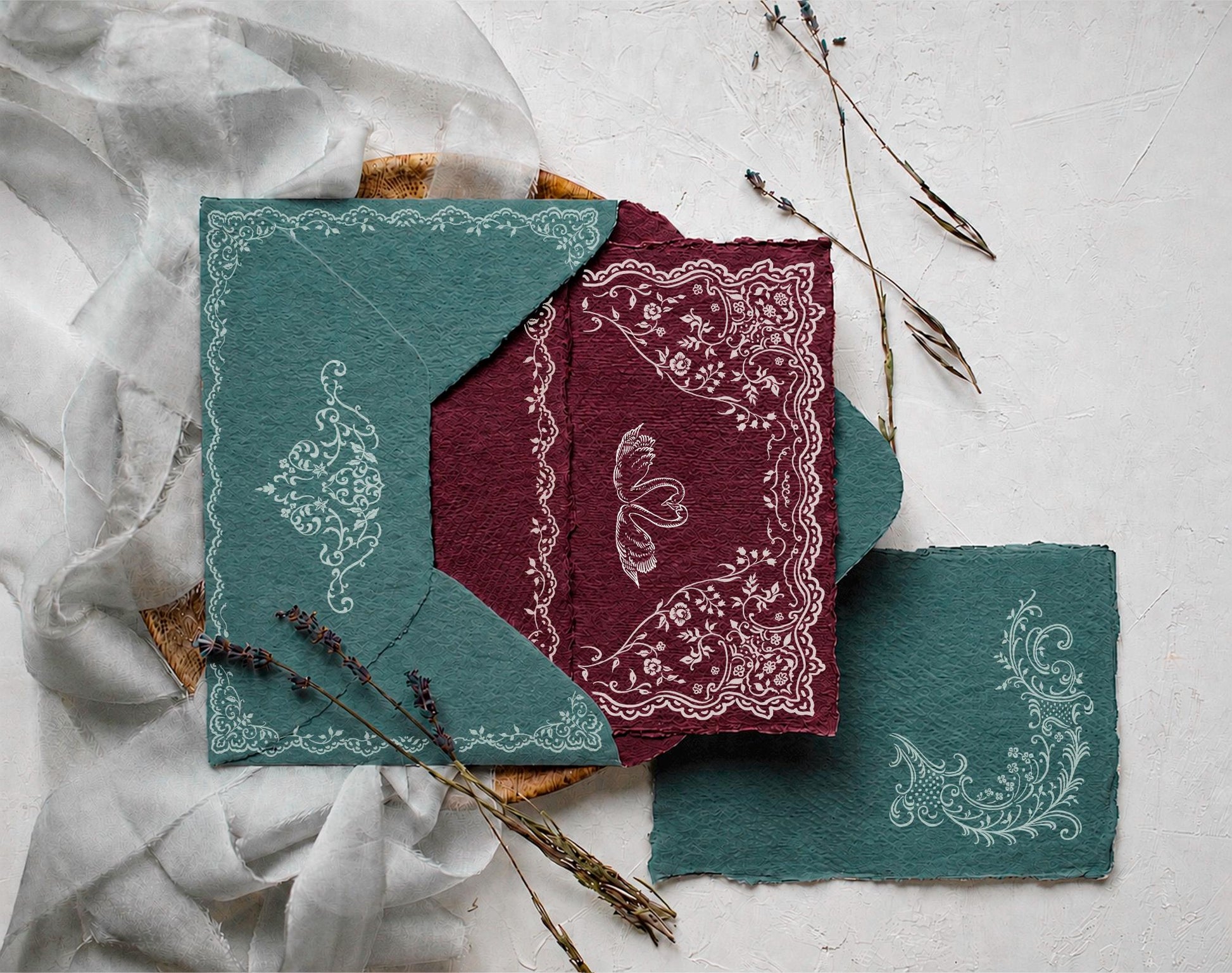 Styled wedding stationery mockup featuring Ivory Lace white ornamental borders on green and burgundy handmade paper.